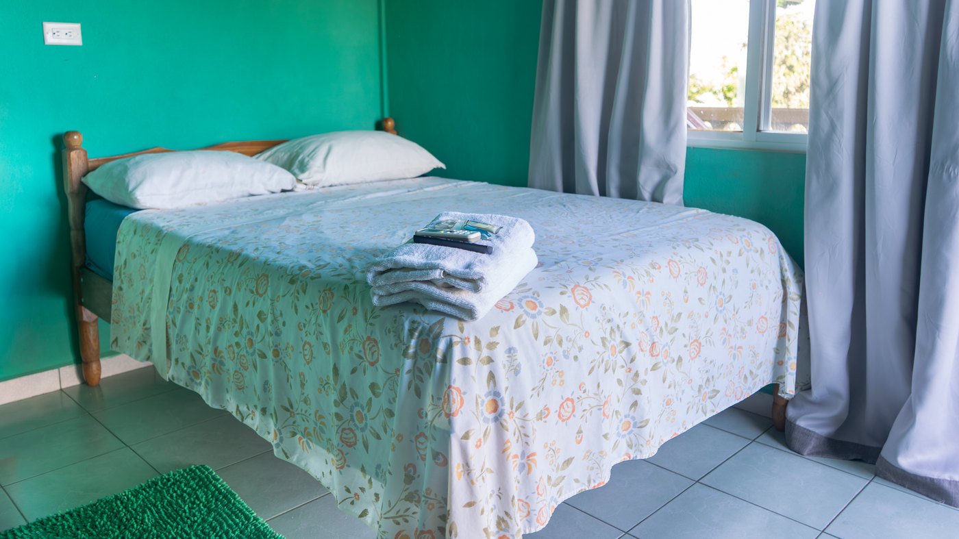 A guest room with floral bedding, turquoise walls, and a sunlit window.